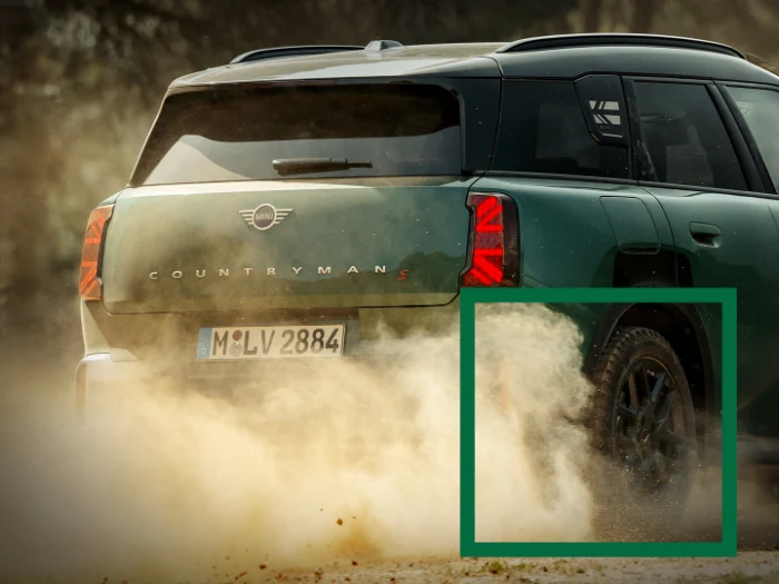 Tył zielonego MINI Countryman w dynamicznej jeździe, unoszący się kurz za autem