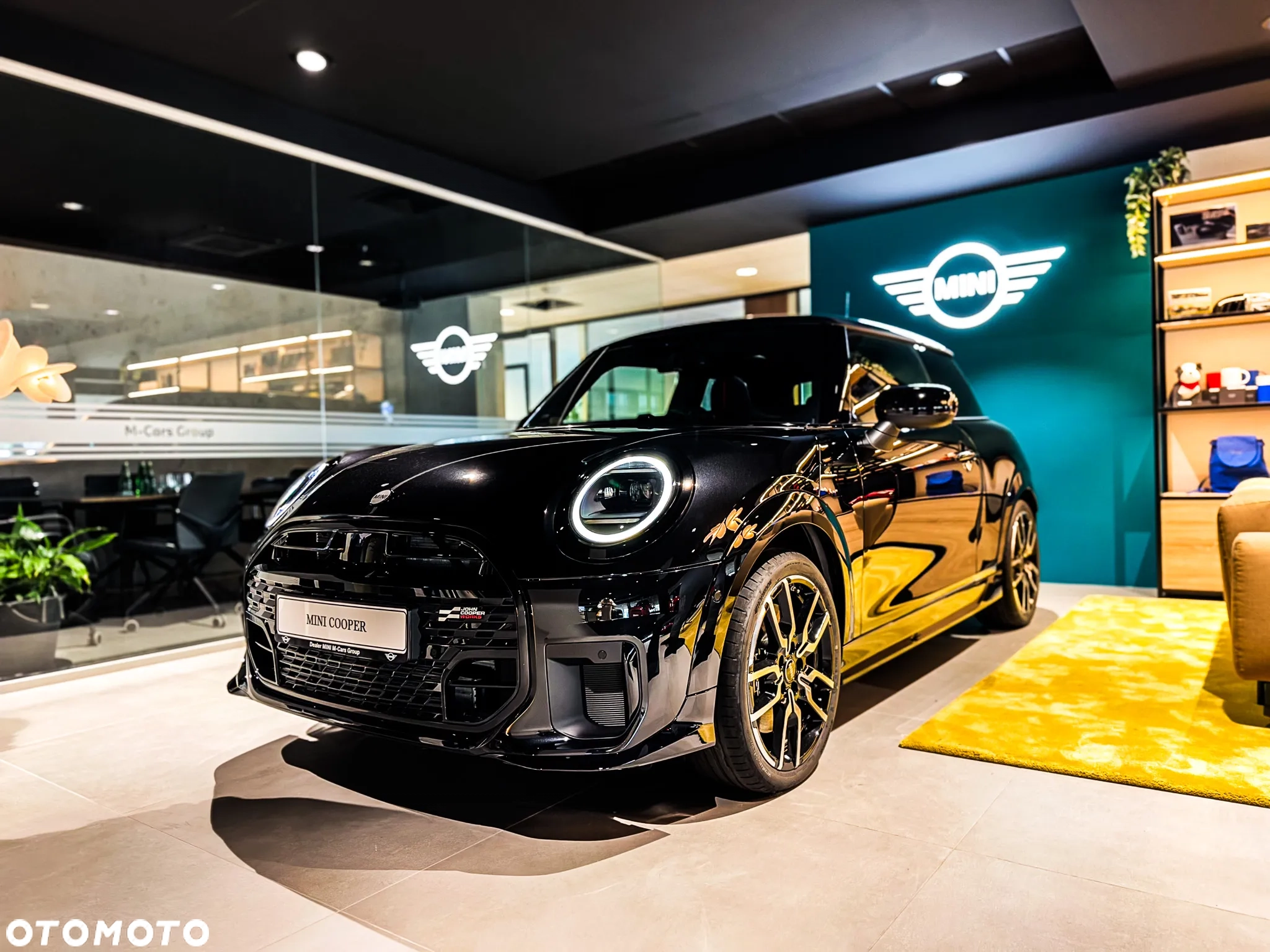 Czarny MINI Cooper na ekspozycji w salonie MINI M-Cars Kraków, podświetlane logo MINI w tle. Samochody MINI Kraków, Małopolska