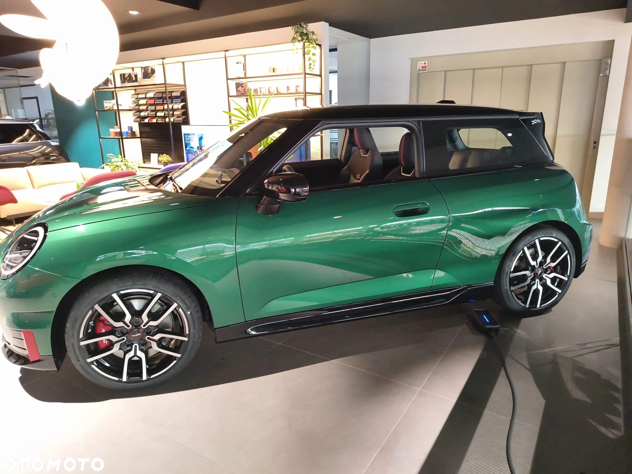 Zielone MINI na ekspozycji w salonie, widoczny kabel ładowania i sportowe felgi. MINI M-Cars Kraków, samochody MINI, Małopolska