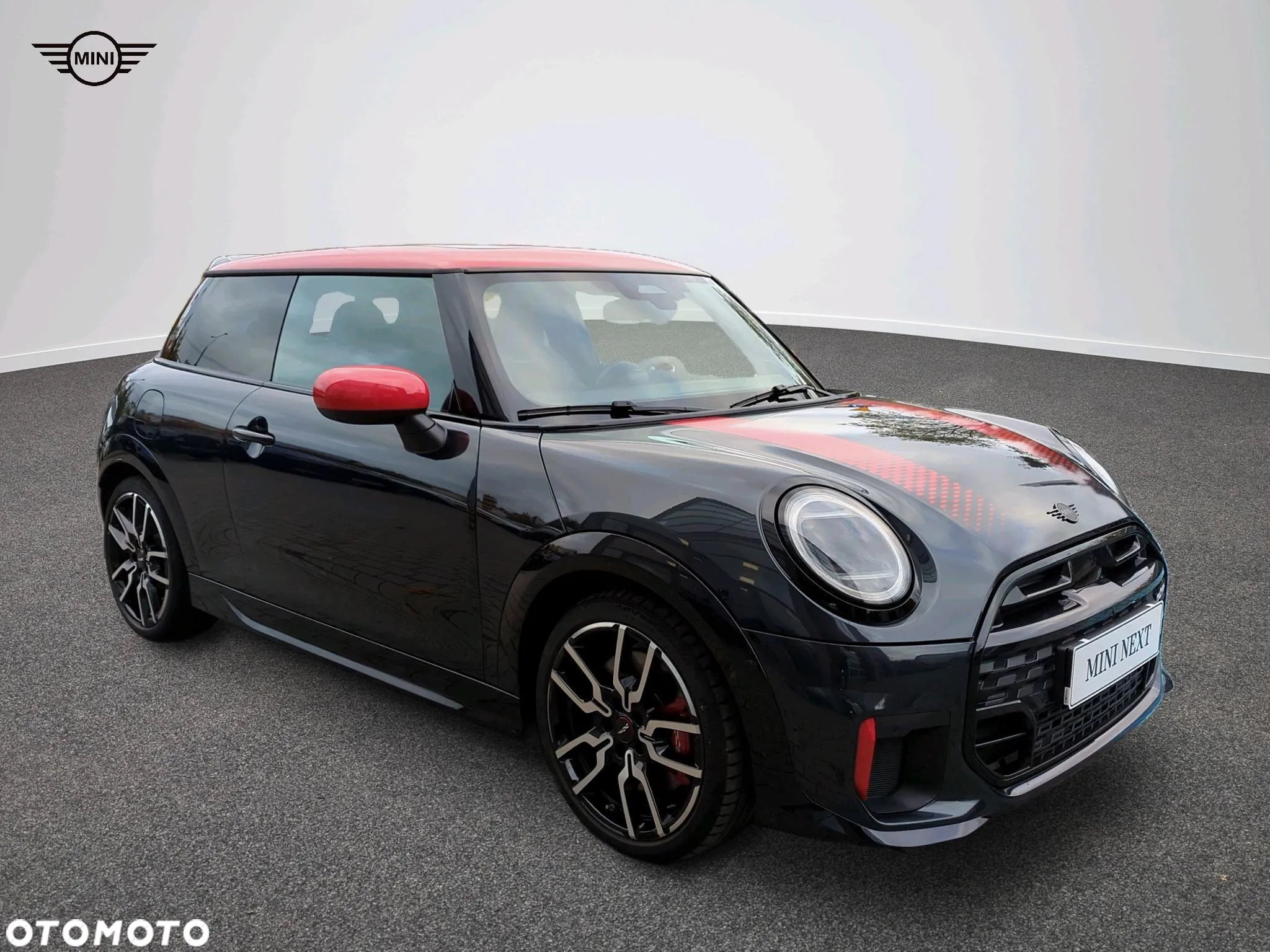 Ciemne MINI Cooper z czerwonym dachem i czerwonymi lusterkami, ujęcie przód-bok na placu. MINI M-Cars Kraków, Małopolska