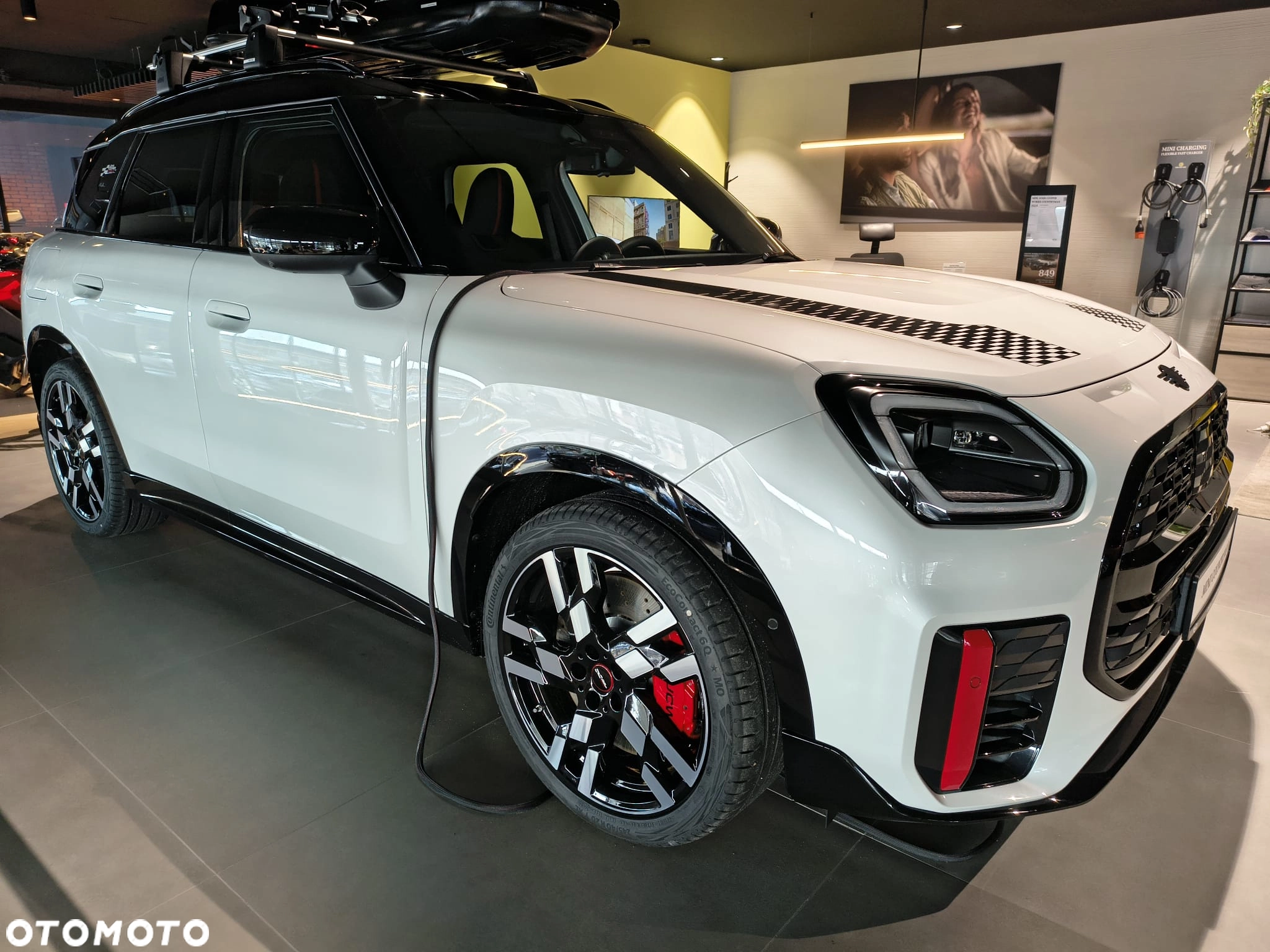 Białe MINI Countryman z boxem dachowym na ekspozycji w salonie – gotowe na wyjazdy. Akcesoria MINI Kraków, MINI M-Cars Kraków, Małopolska