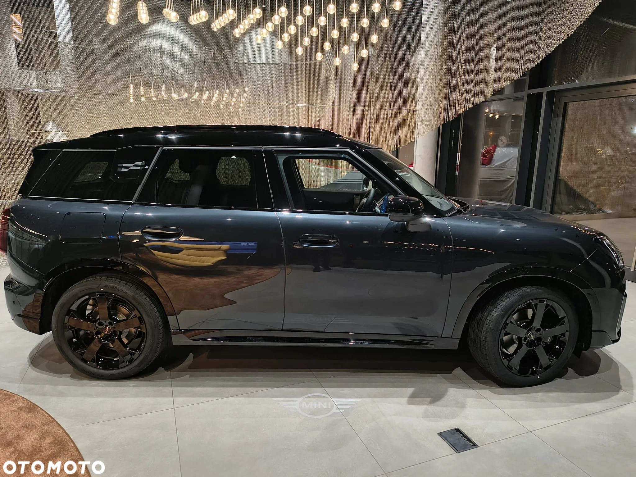 Ciemne MINI Countryman w ujęciu bocznym w salonie, czarne felgi i mocna linia nadwozia. MINI M-Cars Kraków, Małopolska