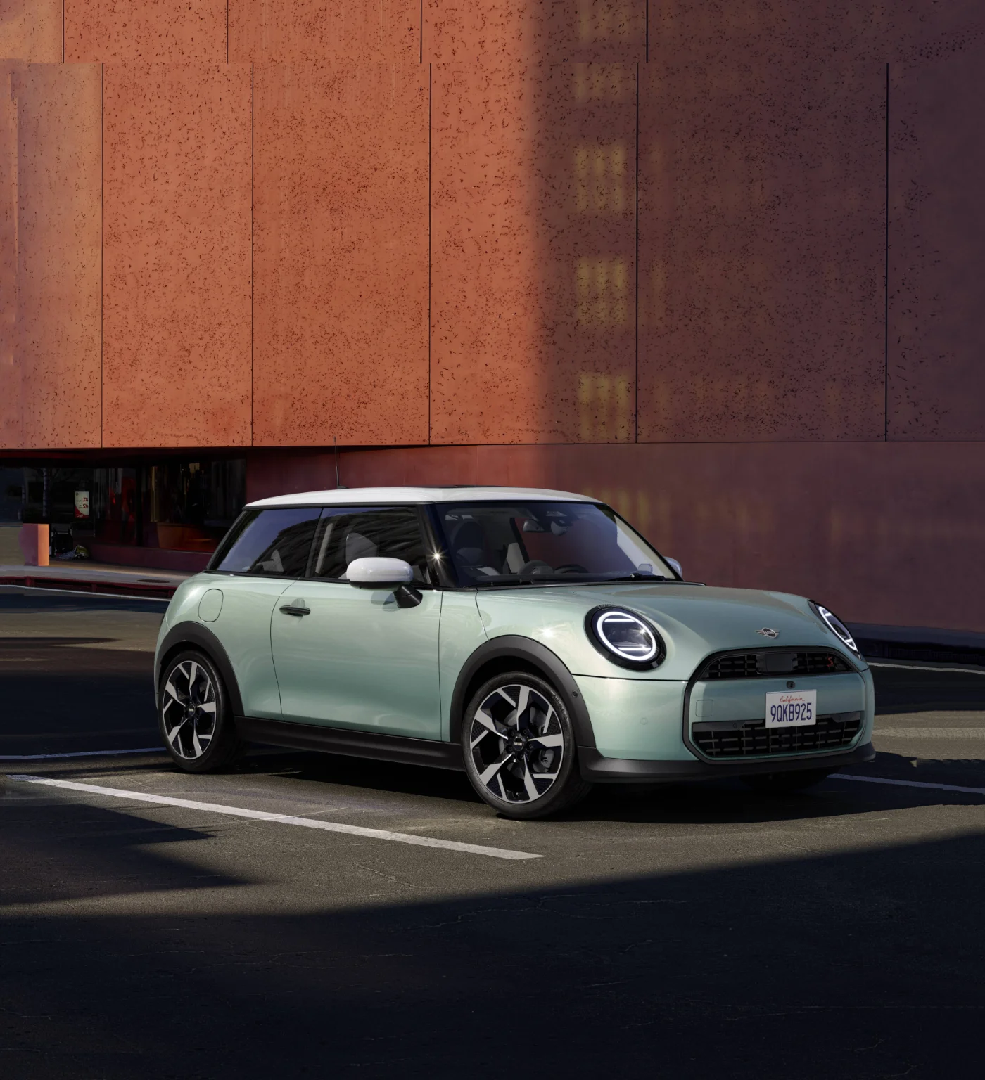 Nowe MINI Cooper ONE F66 widziane z przodu i boku na miejskim parkingu. Charakterystyczne reflektory LED i kompaktowa sylwetka modelu MINI.