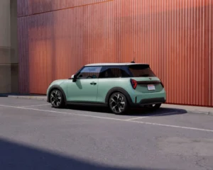 Nowe MINI Cooper ONE F66 w kolorze miętowym zaparkowane przy nowoczesnej elewacji budynku. Miejski design i kompaktowe nadwozie MINI.