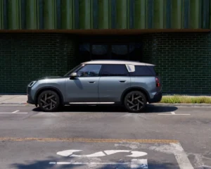 Profil boczny nowego MINI Countryman ONE zaparkowanego przy nowoczesnym budynku. Przestronny SUV marki MINI.