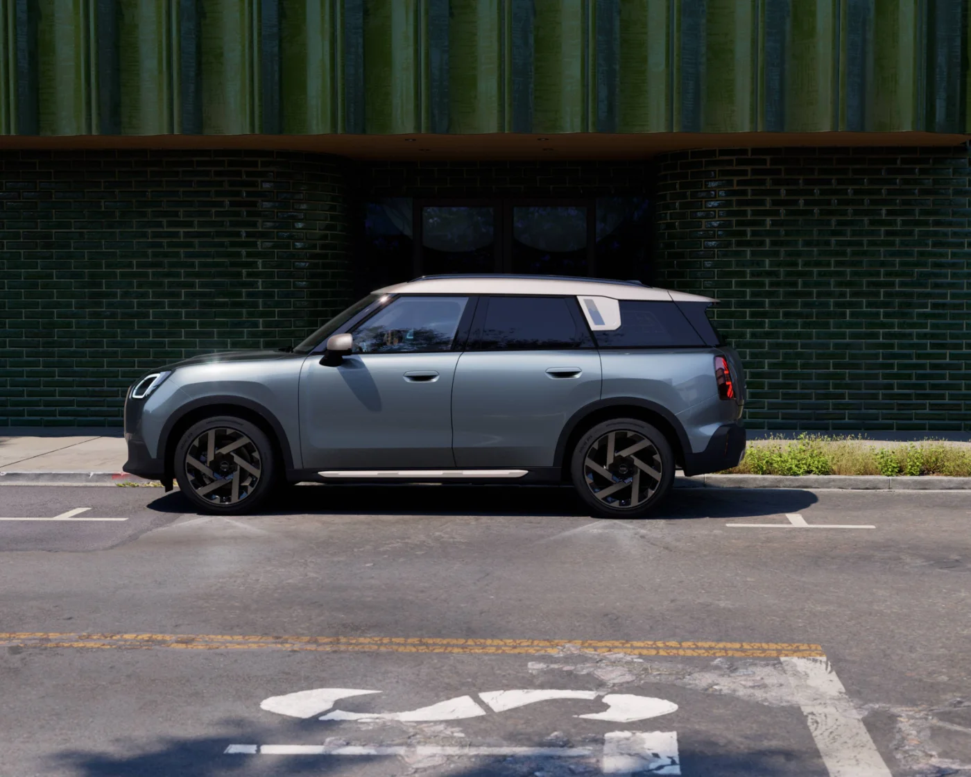Profil boczny nowego MINI Countryman ONE zaparkowanego przy nowoczesnym budynku. Przestronny SUV marki MINI.