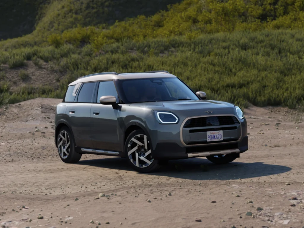 Szary MINI Aceman zaparkowany na szutrowym terenie w otoczeniu zielonych wzgórz. Nowoczesny crossover MINI prezentowany przez M-CARS Kraków, idealny do codziennej jazdy i weekendowych wyjazdów